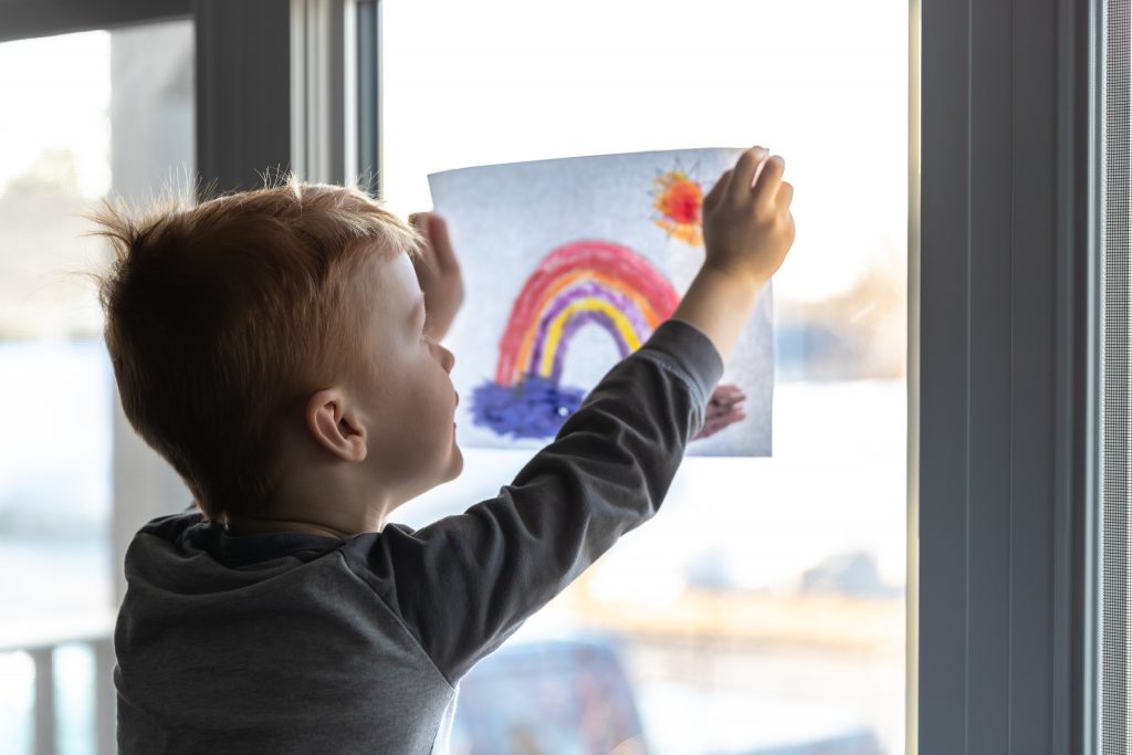 Young Boy sticking his drawing on home window during the Covid-19 crisis