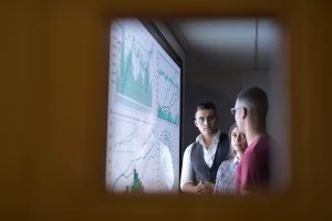 Three colleagues analyzing data displayed on digital wall