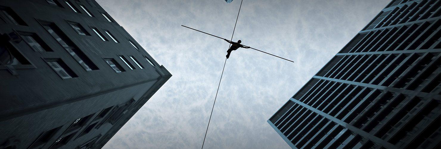 ground view of man tightrope walking across the roofs of two high rise buildings