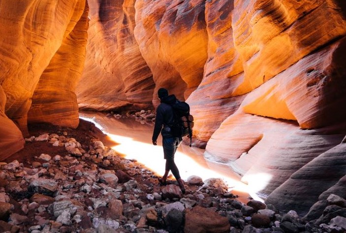 man hiking through red rock caves in Utah