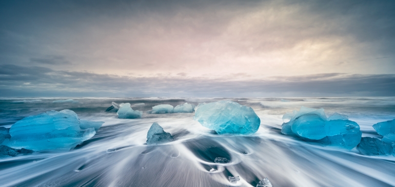 blocks of blue ice on icy sandy beach with waves in rolling in