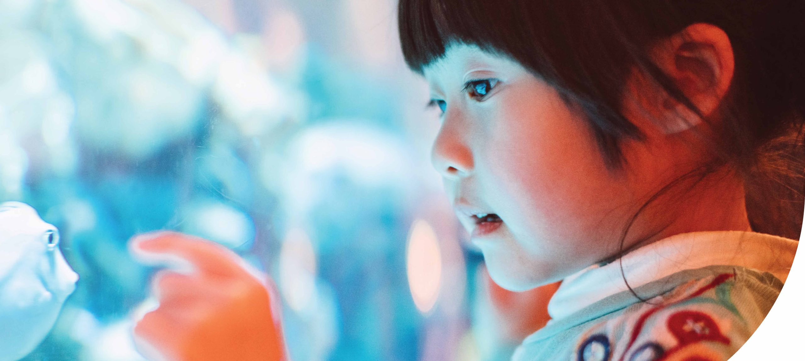 female child of Asian decent trying to touch a fish through the glass of aquarium